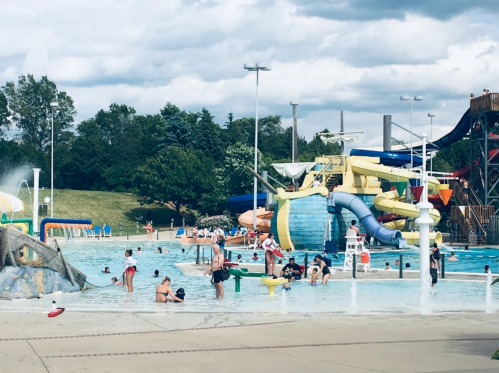 A busy water park with a large pool, water slides, and families enjoying the attractions under a cloudy sky.