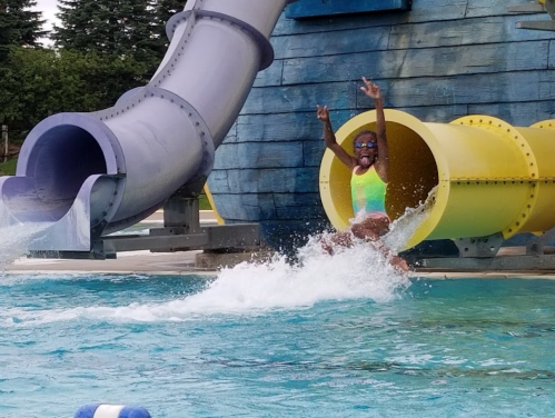 A child joyfully splashes into a pool after sliding down a colorful water slide.