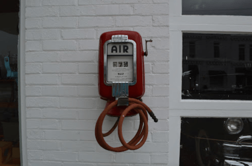Vintage red air pump mounted on a white brick wall, featuring a gauge and a coiled hose.