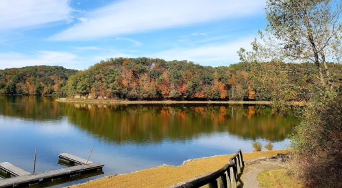 A serene lake surrounded by trees with autumn foliage, reflecting the colorful landscape under a clear blue sky.