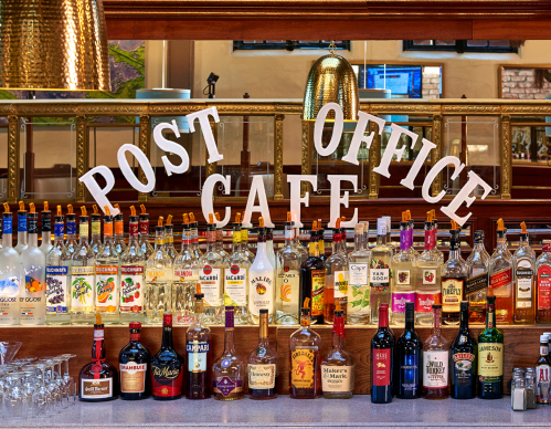 A bar display featuring various bottles of liquor with a sign reading "POST OFFICE CAFE" above them.