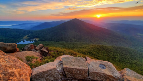 A stunning sunset over rolling mountains, with a serene lake nestled in the valley below.