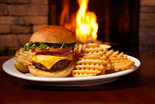 A juicy cheeseburger with lettuce, tomato, and onion, served with waffle fries, against a warm, glowing fireplace backdrop.