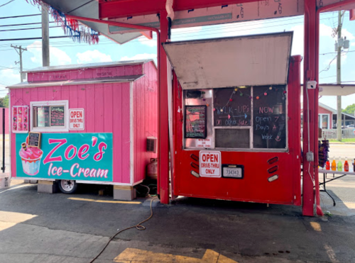 A pink ice cream stand named "Zoe's Ice-Cream" next to a red food truck, both open for business.