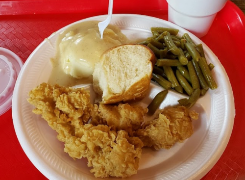 A plate of fried chicken, mashed potatoes with gravy, green beans, a roll, and a drink on a red tray.