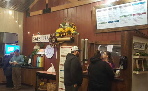 A cozy restaurant counter with a menu, flowers, and customers ordering food in a rustic setting.