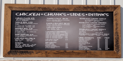 Menu board featuring chicken dishes, sides, drinks, and prices for various meal options.