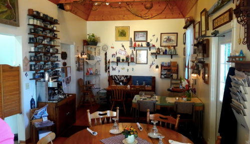 Cozy dining room with wooden tables, vintage decor, and shelves filled with collectibles and kitchenware.