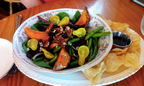 A colorful salad with sweet potatoes, green beans, nuts, and cherry tomatoes, served with a side of crispy chips.