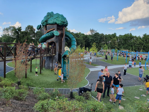 A vibrant playground with a large treehouse slide, children playing, and families enjoying the outdoor space.