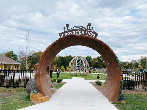 Archway sign reading "Innovation Hills" at a park entrance, with a playground and trees in the background.