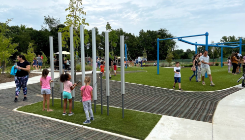 Children play in a park with musical instruments, while adults socialize nearby under a cloudy sky.