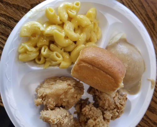 A plate of food featuring macaroni and cheese, fried chicken, a roll, and mashed potatoes with gravy.