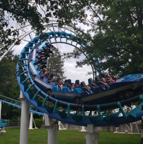 A roller coaster twists through the air with riders enjoying the thrill against a backdrop of trees and cloudy skies.