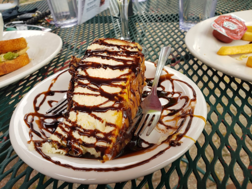 A slice of cake drizzled with chocolate sauce on a plate, with a fork resting beside it.