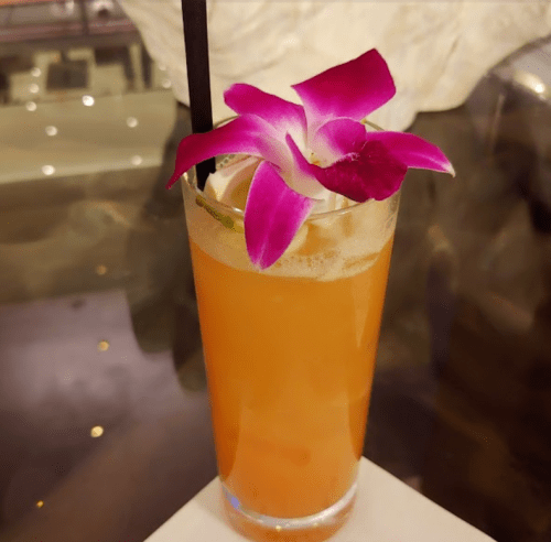A refreshing cocktail garnished with a purple orchid, served in a tall glass with ice.