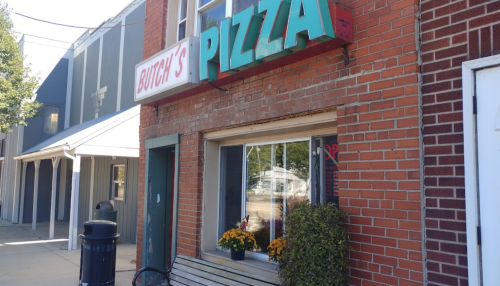Exterior of Butch's Pizza, featuring a brick facade and colorful signage, with flowers by the window.