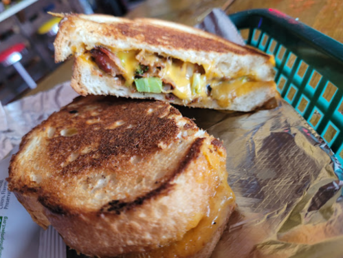 A toasted sandwich with melted cheese, bacon, and green onions, served in a green basket.
