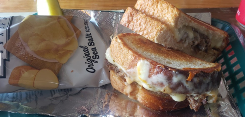 A grilled cheese sandwich with melted cheese and a side of sea salt potato chips on a green tray.
