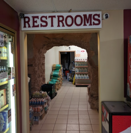 Sign for "Restrooms" above an entrance leading to a rocky passageway with shelves of products on either side.