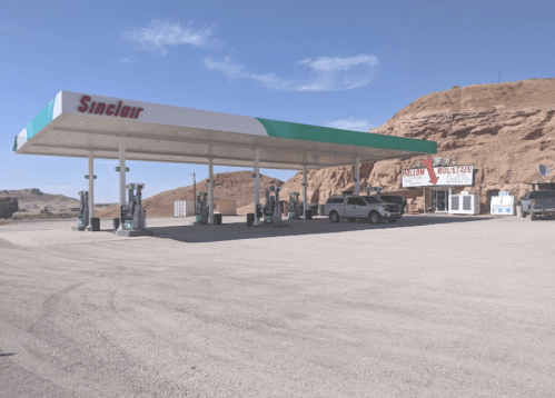 A Sinclair gas station with pumps, surrounded by rocky terrain and a clear blue sky.