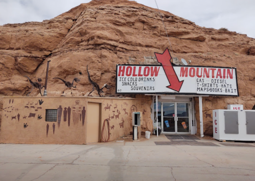 A rustic gas station and souvenir shop at the base of a rocky mountain, featuring a large sign and desert landscape.