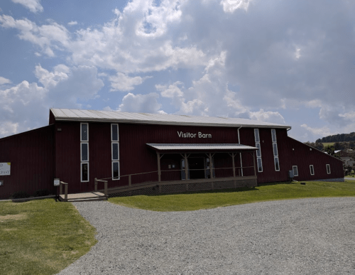 Red barn labeled "Visitor Barn" with a porch, set against a cloudy sky and grassy area.