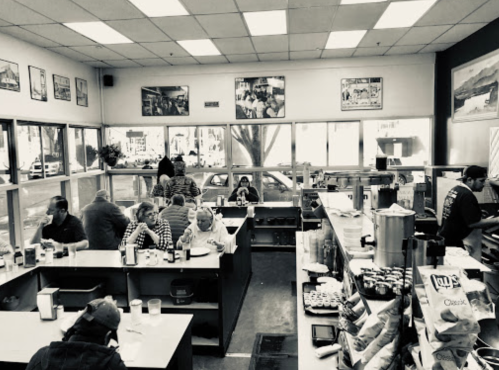 A busy diner with patrons seated at tables, a counter with drinks, and black-and-white decor featuring vintage photos.