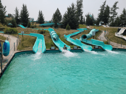 A water park featuring multiple turquoise water slides and a pool, with a person sliding down one of the slides.