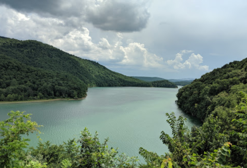 A serene lake surrounded by lush green hills under a cloudy sky.