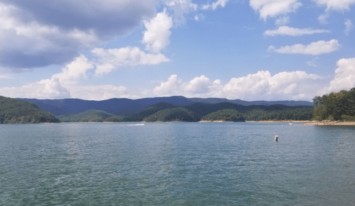 A serene lake surrounded by mountains under a partly cloudy sky, with gentle waves and a boat in the distance.