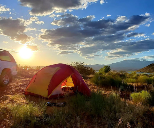 A colorful tent set up in a grassy area at sunset, with mountains and clouds in the background.