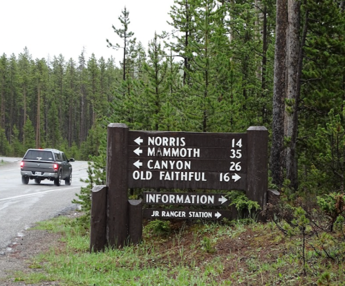 A wooden signpost with directional arrows indicating distances to Norris, Mammoth, Canyon, and Old Faithful.