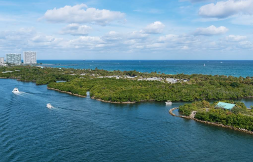 Aerial view of a lush green island surrounded by blue water, with boats navigating through the channels.