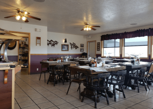 Cozy restaurant interior with wooden tables, chairs, and ceiling fans, featuring a warm, inviting atmosphere.