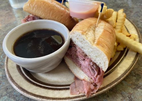 A plate with a sliced roast beef sandwich, a small bowl of dipping sauce, and crinkle-cut fries.
