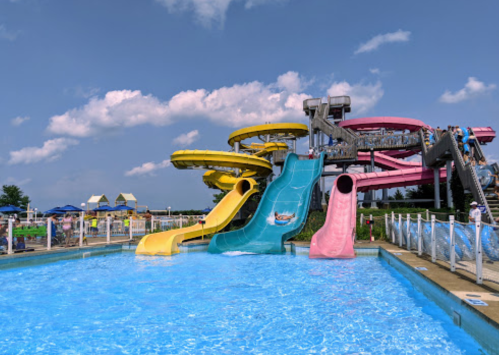 Colorful water slides tower over a blue pool under a clear sky, with people enjoying the water park.