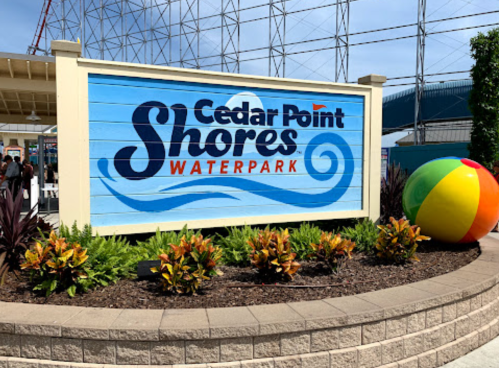 Sign for Cedar Point Shores Waterpark with colorful beach ball and vibrant landscaping in the foreground.
