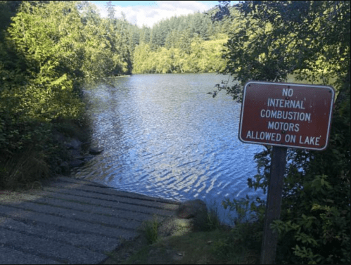 A serene lake surrounded by trees, with a sign stating "No internal combustion motors allowed on lake."