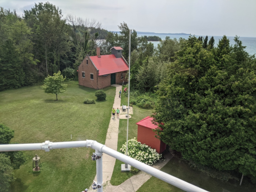 Aerial view of a red-roofed building surrounded by greenery, with a path leading to the water in the background.