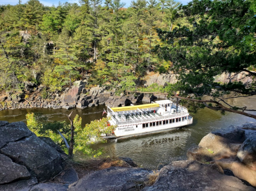A white riverboat navigates a winding river surrounded by rocky cliffs and lush greenery.