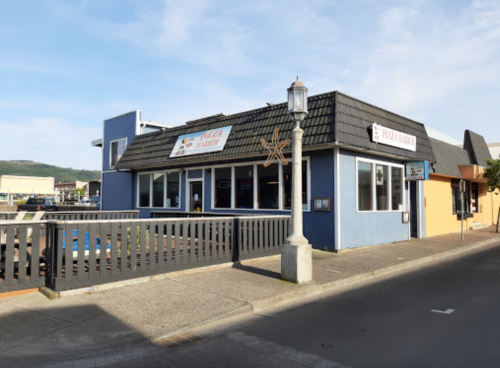 A blue restaurant with a sloped roof, featuring large windows and a sign that reads "Pizza Harbor."