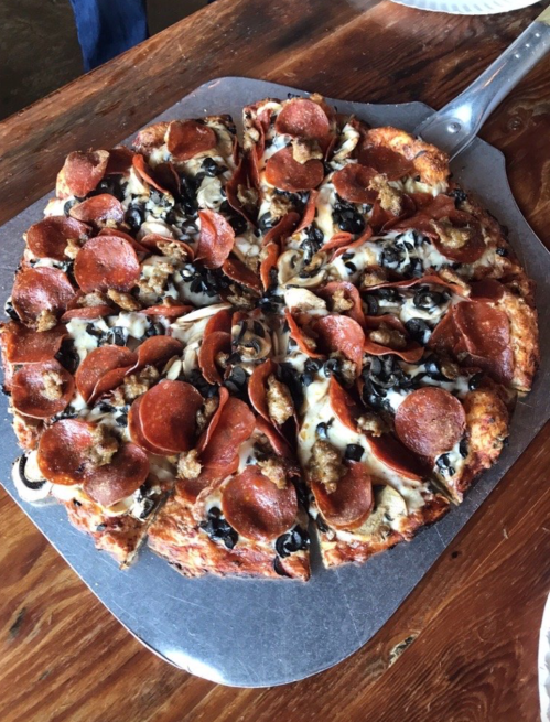 A freshly baked pizza topped with pepperoni, sausage, and black olives, served on a metal pizza tray.