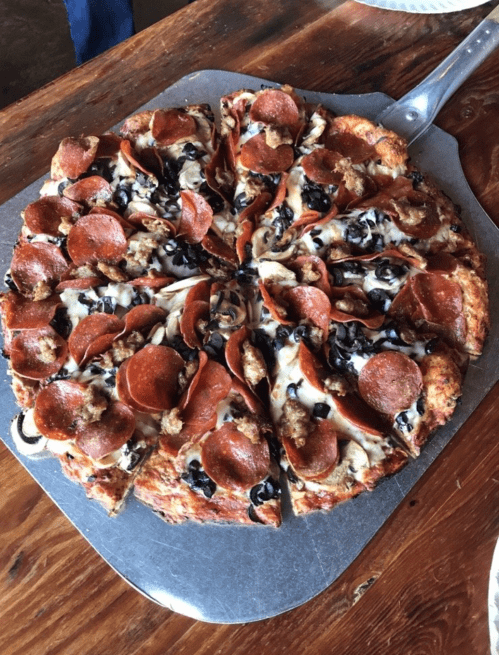 A freshly baked pizza topped with pepperoni, sausage, and black olives, served on a metal pizza tray.