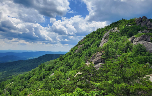 Lush green mountains under a partly cloudy sky, with rocky outcrops and distant hills visible in the background.