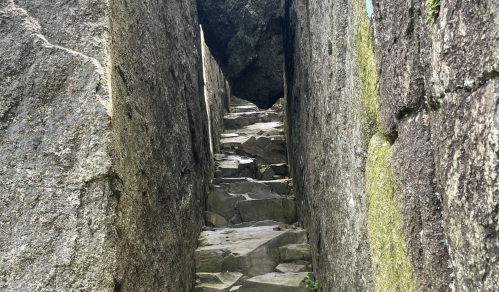 Narrow stone pathway between tall rock walls, leading upward through a rugged landscape.