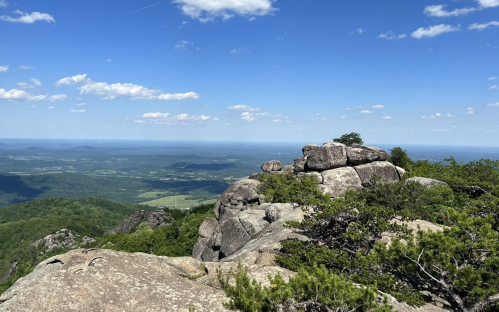 A rocky outcrop overlooks a lush green valley under a bright blue sky with scattered clouds.