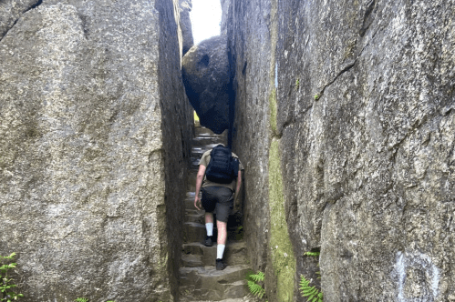 A hiker ascends stone steps between two large rock formations in a narrow passageway.