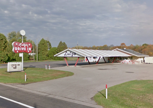 A retro drive-in restaurant with a large sign, featuring a covered outdoor seating area and green surroundings.