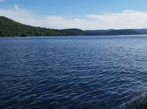 A serene lake surrounded by green hills under a clear blue sky, with gentle ripples on the water's surface.